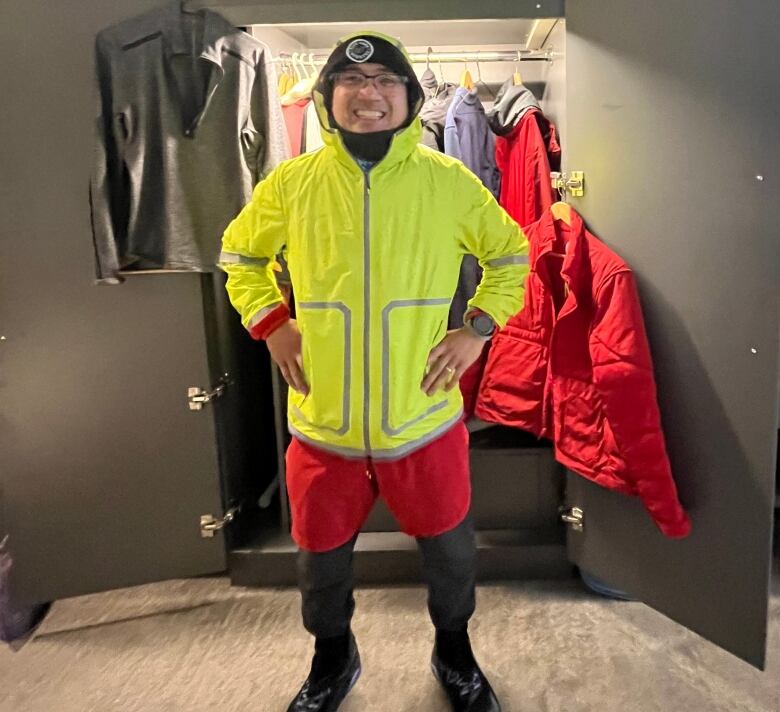 Person in bright yellow jacket stands in front of a closet.