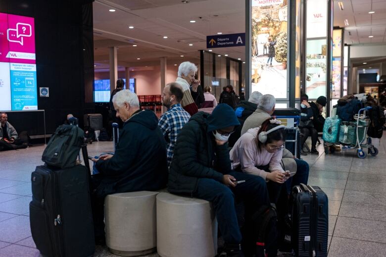 A group of people sit on chairs staring at their cellphones.