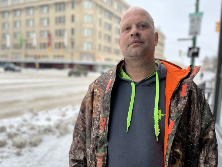 A man in a camouflage jacket stands outside the corner of a busy intersection.