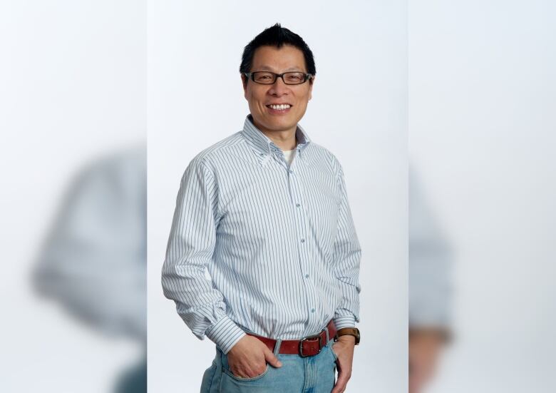 A man wearing black glasses and a blue striped shirt poses for the camera.