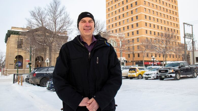 A man wearing a toque stands in a city's downtown surrounded by snow.