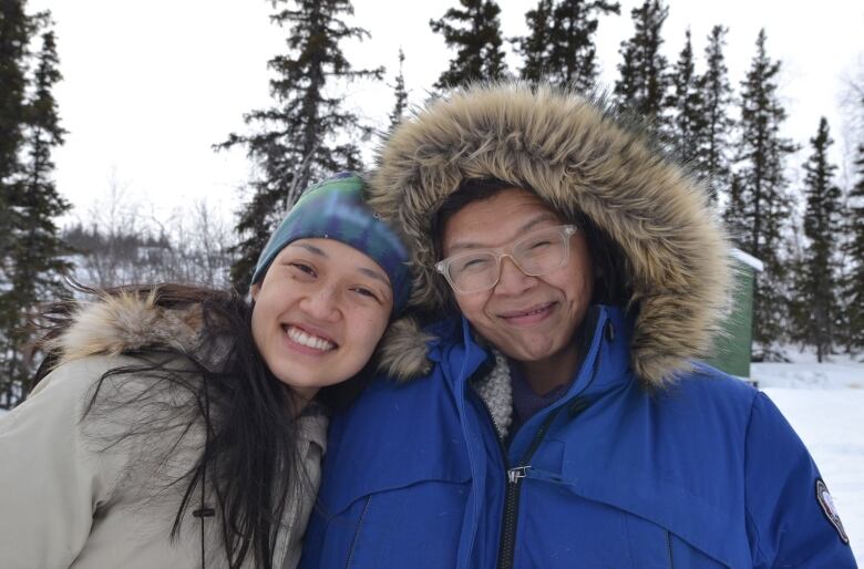 Two smiling people in snowy forest.