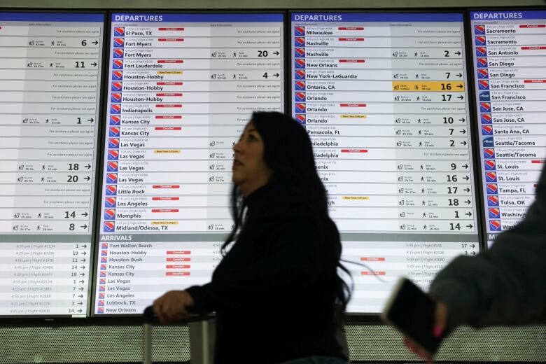 A person walks in front of an airport departures board showing many delayed and cancelled flights.