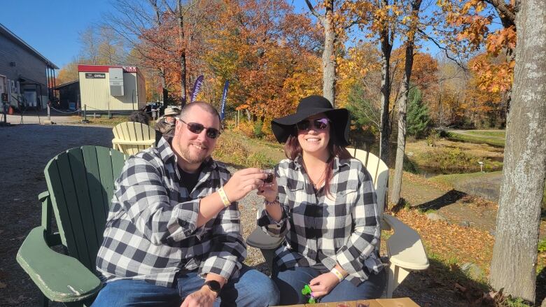 A man and woman in black and white flannel shirts sit with sunglasses.