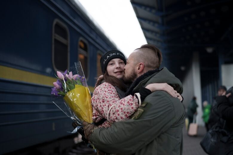 A soldier embraces a child at a train station.