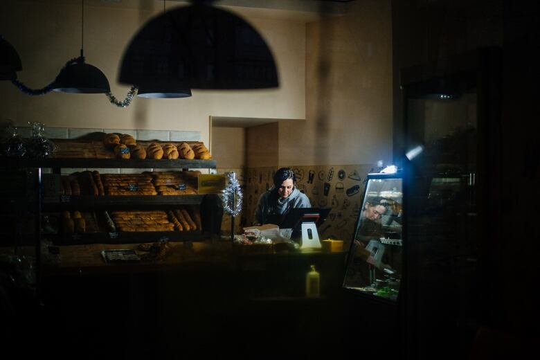 A person sells bread in a dimly lit store during a blackout.