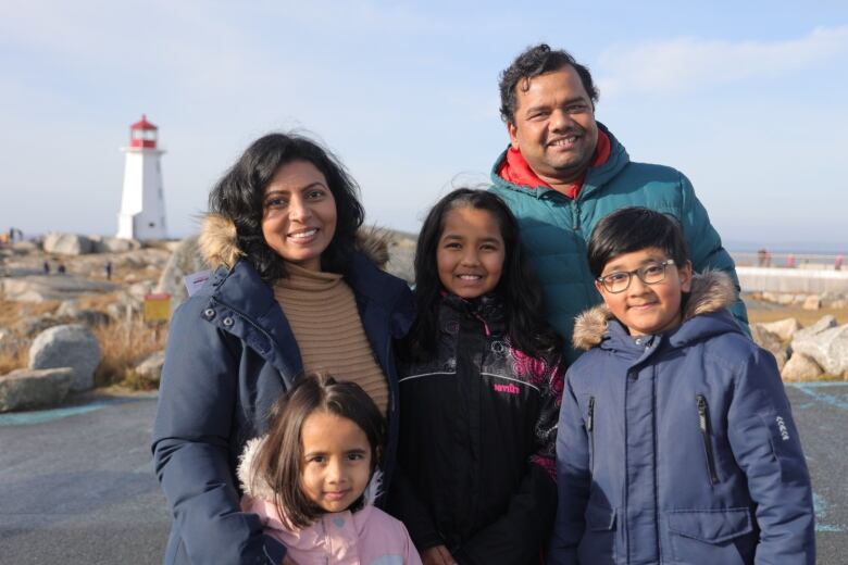 A family stands and smiles in front of the Peggys Cove lighthouse