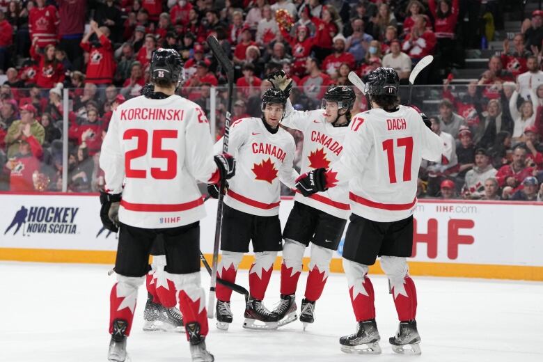 Five Canadian hockey players gather in the middle of the ice to celebrate a goal.