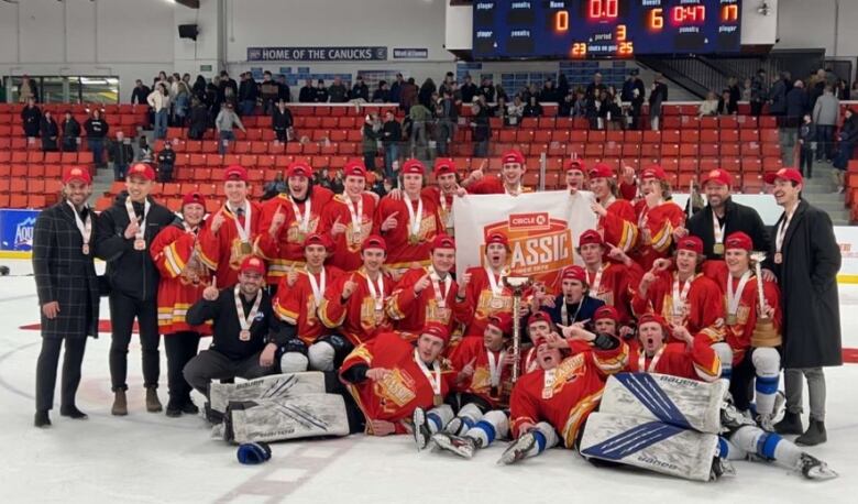 A hockey team in red jerseys and wearing medals poses as a group on the ice inside an arena.