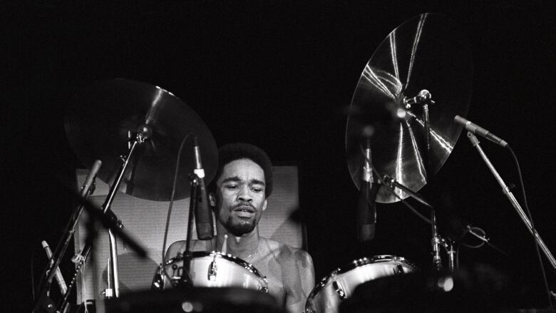 A black and white image shows a drummer playing the drums on stage.