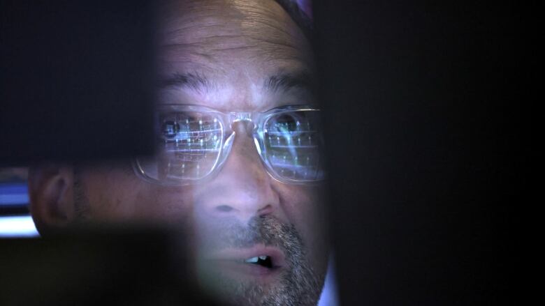 Stock market trader with market boards reflected in his glasses.