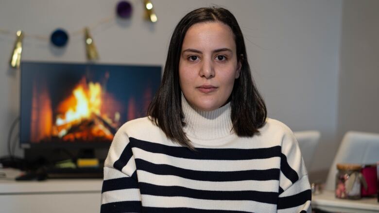 A woman in a striped sweater sits in her small apartment.