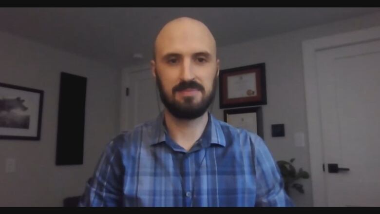 Man with dark brown beard and blue plaid shirt looks into camera.