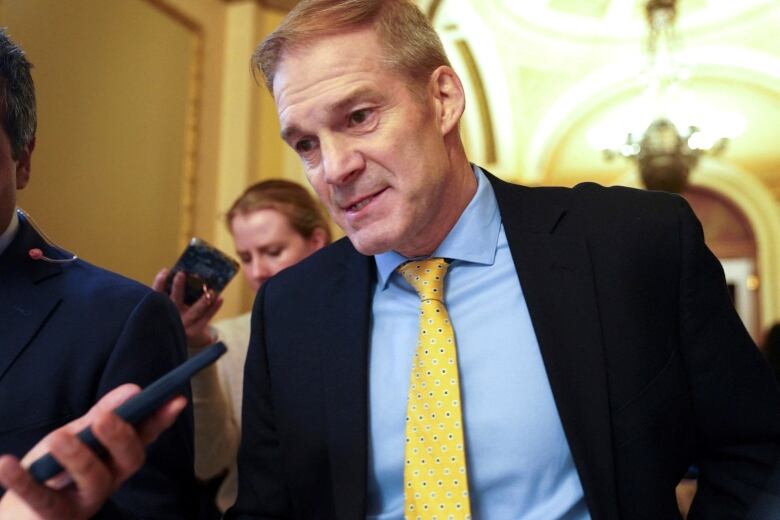 A man in a suit and tie is shown while a reporter holds out a recording device.