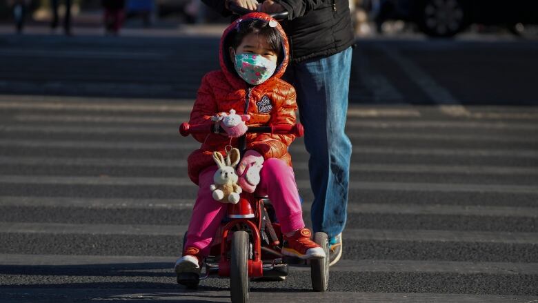 A child wearing a face mask rides a tricycle in Beijing, China.