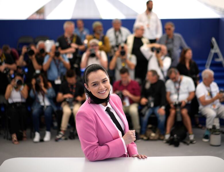 A woman in a pink suit poses and smiles as photographers take pictures of her.