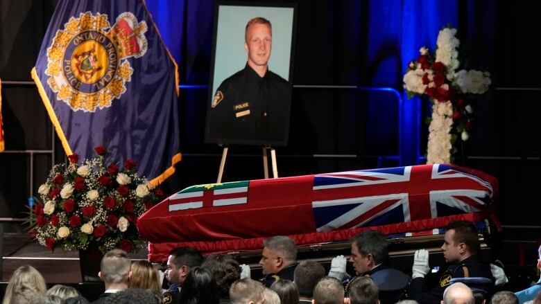 A casket carrying body of police officer is carried by pallbearers after a funeral service at an arena.