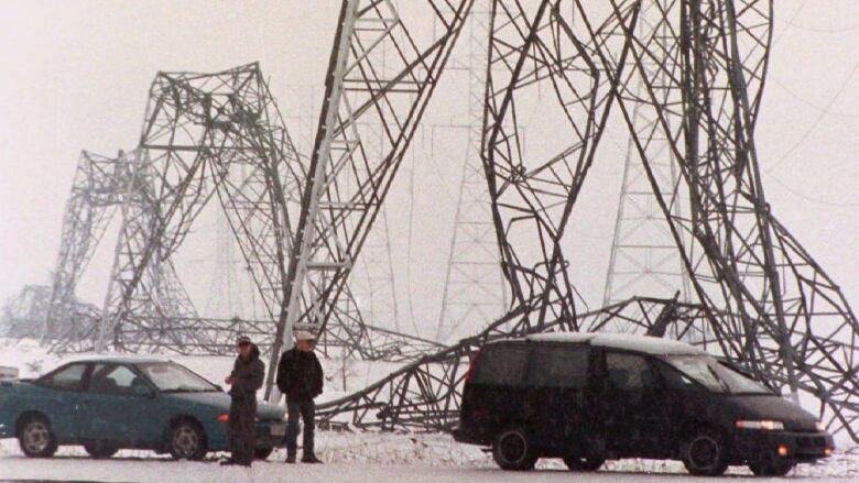 Two men stand amid crumbled electrical structures.