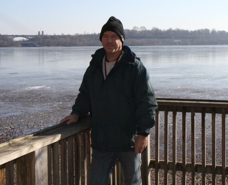 A man stands on a wooden lookout in front of a large body of water. 