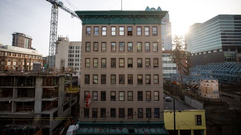 The front facing windows of a single room occupancy hotel and a flat, green roof are seen next to a crane and construction site on Vancouver's Downtown Eastside.