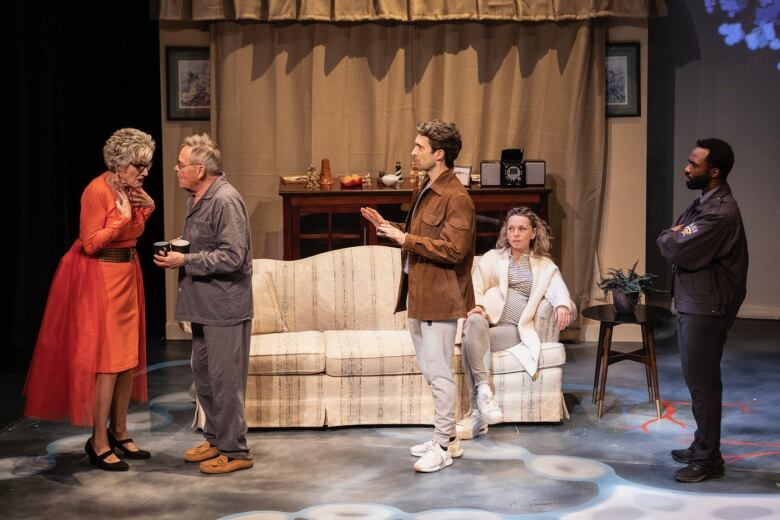 An older couple, a younger couple and a police officer stand on a stage while what appears to be an emotional conversation plays out.