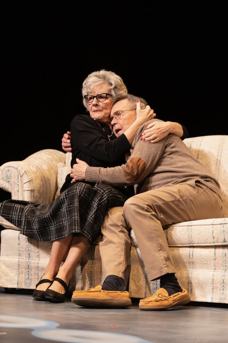 An older couple embrace while sitting on a couch.