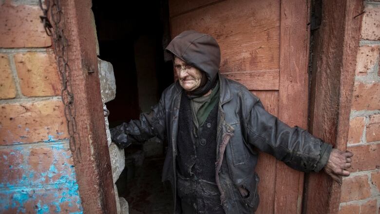 A distraught looking individual stands in the doorway of a home. 