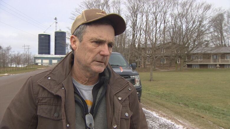 MLA Jamie Fox sands in a brown cap and jacket on the side of the road for an interview with CBC News.