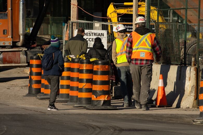 Construction workers are pictured on a site with orange pylons lining the road.