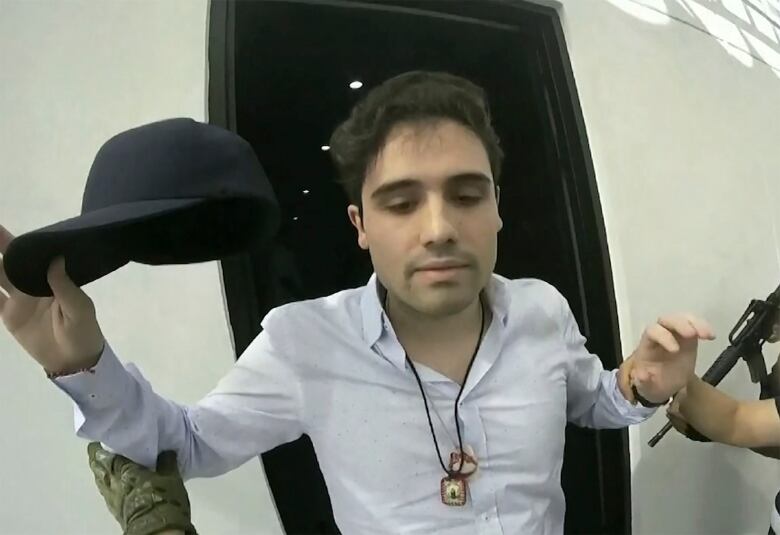 Man in while collared shirt holding baseball cap mements before his detention.