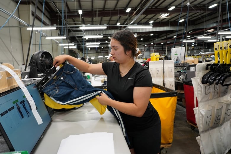 A woman folds clothes in a warehouse.