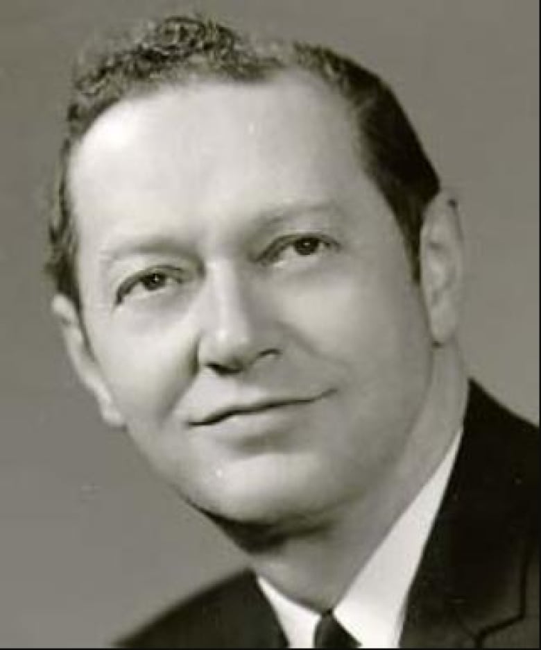 A tight portrait shot of a man in suit and tie with short, wavy hair.