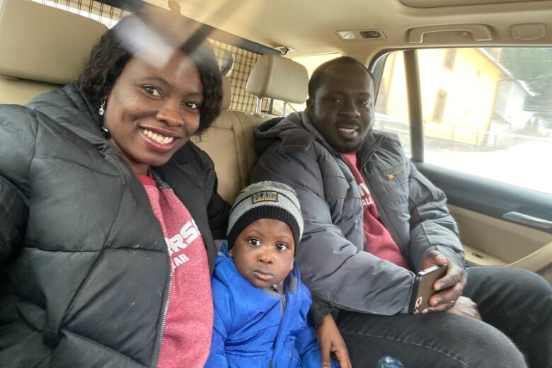 A woman and a man with a small child in between them. They are in the backseat of a vehicle.