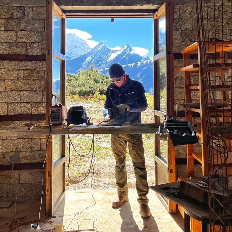 A man working with metal with a Nepalese mountain range in the background.