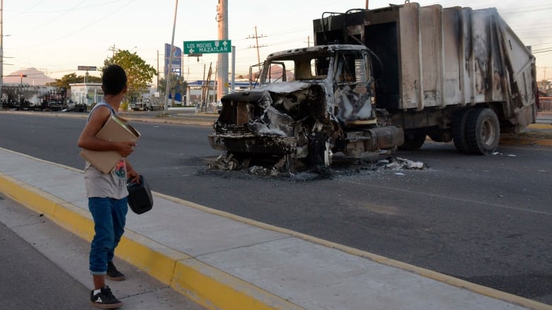 A man walks by a burned truck