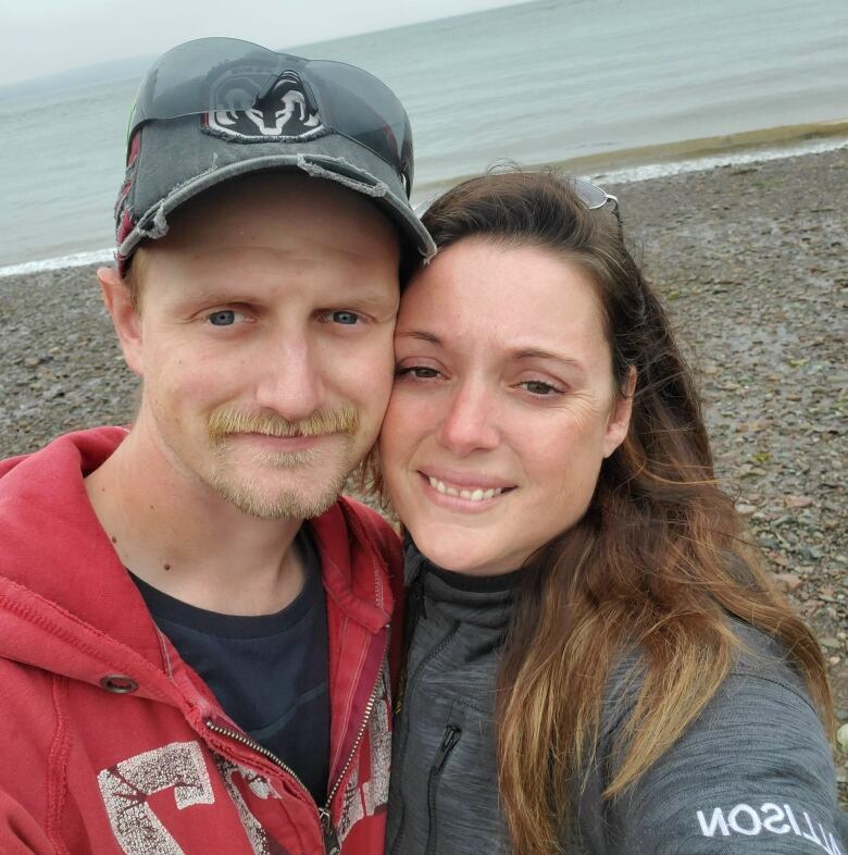 A man and woman smile at the camera on a beach.