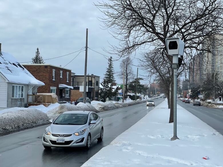 A camera on a post in the median of a residential street.