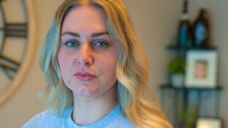 A woman with big green eyes and blonde hair solemnly looks forward. A picture frame holds the image of a woman in the crushed background. 