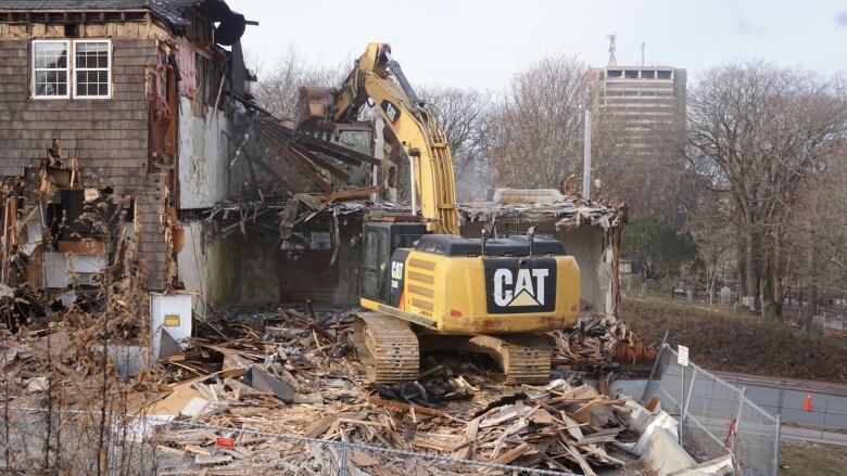 The inside of a building being demolished, we see both floors and the excavator as it works its way through the rubble. 