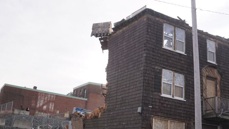 An excavator tears down an old, shingle-sided multi-storey building