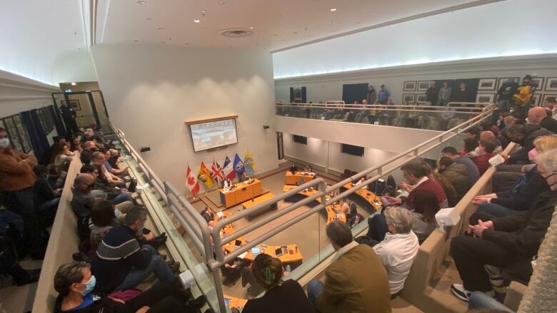 People sit in the upstairs gallery of a city hall council chamber.