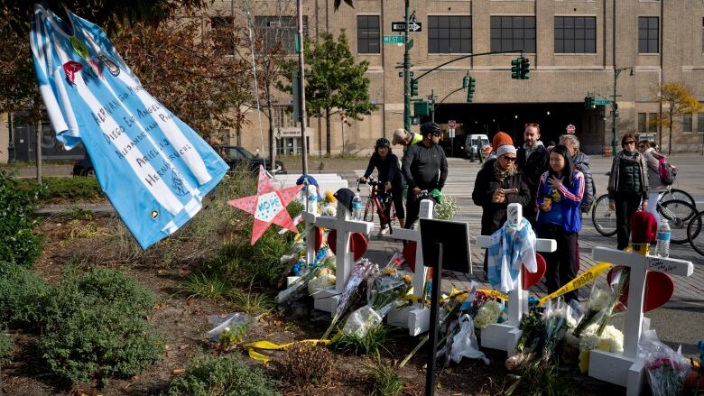 Flowers, crosses and a flag are displayed in a garden, with several onlookers nearby.