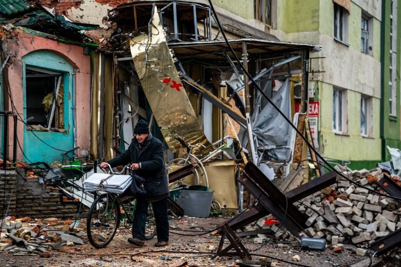 Wires and other detritus hang down from a heavily damaged building, while bricks litter the ground.