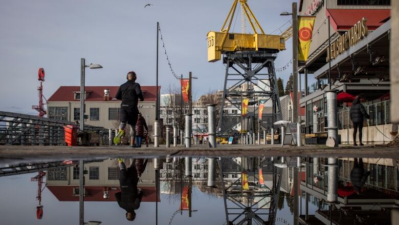 A man framed by nautically-themed retail spaces runs along the boardwalk in the Shipyards District in North Vancouver.