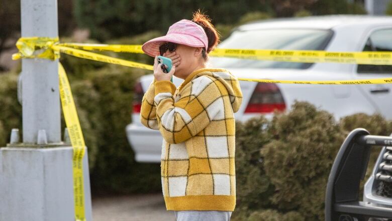 A frantic woman holds her crying face as she stands in front of a house surrounded by police tape.