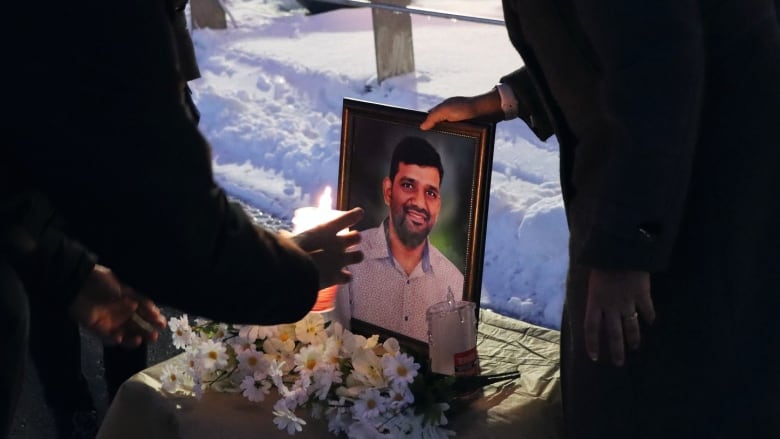 Students place plastic candles in front of a photograph of an international student from India who was killed in a December 2022 house fire in Sydney, N.S.