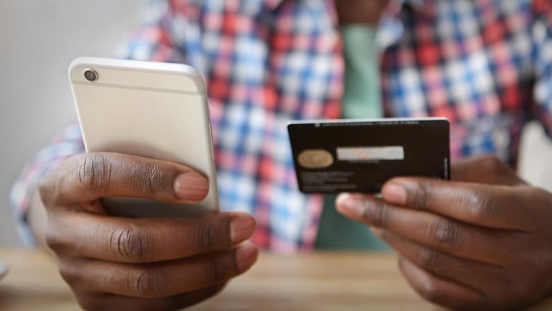 An anonymous person holding a smartphone and a credit card.