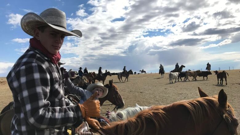 A teenage boy is riding a horse on a ranch. There are cattle and other horses in the background.