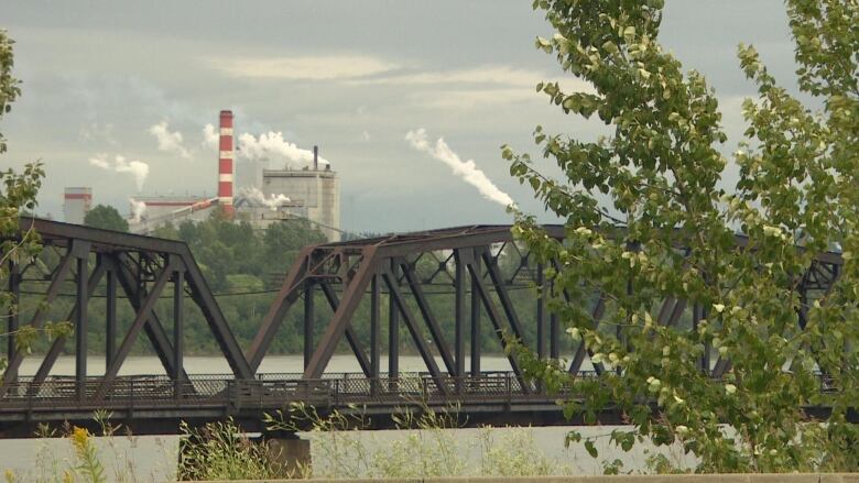 Smoke billows from a mill in the background, with a bridge in the foreground.