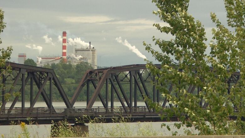 Smoke billows from a mill in the background, with a bridge in the foreground.